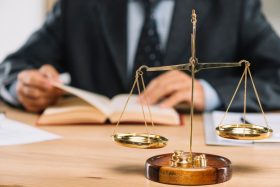 escala-de-justica-de-ouro-na-frente-do-livro-de-leitura-de-advogado-na-mesa_23-2147898544